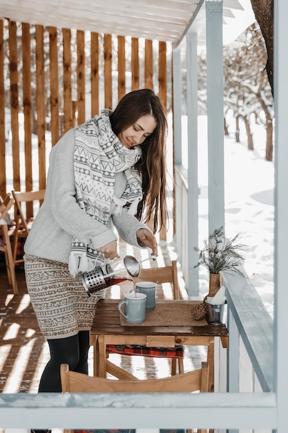 La donna sta versando il tè caldo sulla terrazza durante l'inverno.