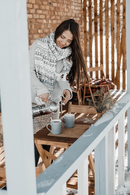 La donna sta versando il tè sulla terrazza durante l'inverno.