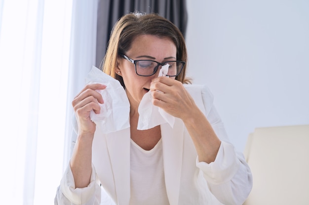 La donna starnutisce nel fazzoletto, la donna d'affari si è ammalata in ufficio, con sintomi di malattie respiratorie. Raffreddore stagionale, allergia stagionale, stagione influenzale, pandemia