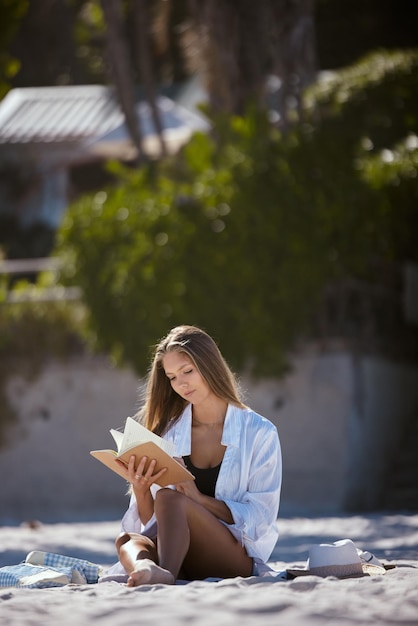 La donna sulla spiaggia che legge il libro e viaggia si rilassa nella natura durante le vacanze estive con pace e calma La giovane donna è all'aperto con un romanzo per leggere le vacanze al mare e rilassarsi al sole