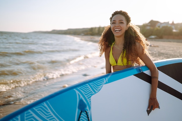 La donna surfista cammina con una tavola sulla spiaggia sabbiosa Sport estremi Viaggia lo stile di vita del fine settimana