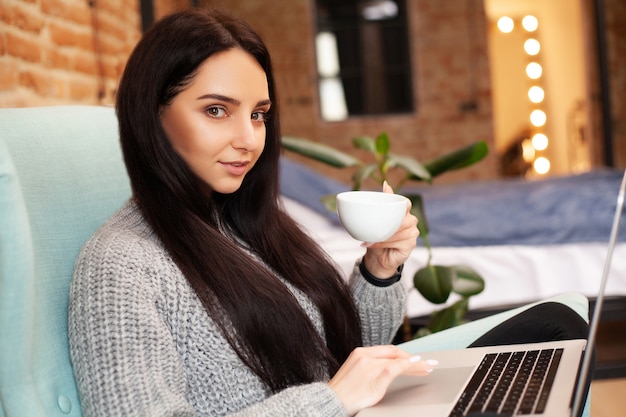 La donna sveglia resta a casa e lavora al computer portatile a bere il caffè