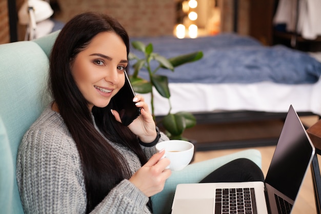 La donna sveglia resta a casa e lavora al computer portatile a bere il caffè