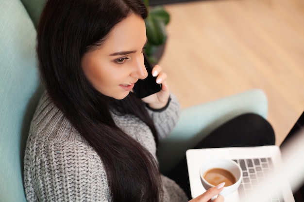 La donna sveglia resta a casa e lavora al computer portatile a bere il caffè