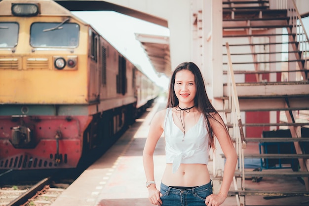 La donna sveglia sta sulla ferrovia con lo sfondo sfocato del treno alla stazione ferroviaria in stile vintage