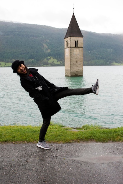 La donna tailandese asiatica del viaggiatore viaggia e posa per scattare una foto alla torre sommersa della chiesa del lago di Resia nel profondo del lago di Resias nella valle del TrentinoAlto o in Alto Adige a Bolzano o nella città di Bolzano in Italia