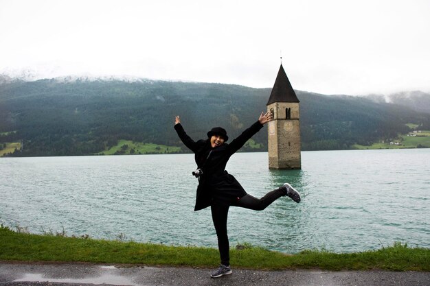 La donna tailandese asiatica del viaggiatore viaggia e posa per scattare una foto alla torre sommersa della chiesa del lago di Resia nel profondo del lago di Resias nella valle del TrentinoAlto o in Alto Adige a Bolzano o nella città di Bolzano in Italia