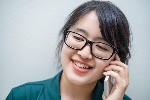 La donna tailandese del primo piano usa lo smartphone su un muro bianco Ragazza asiatica chiama il telefono per lavoro Parlando sul telefono cellulare