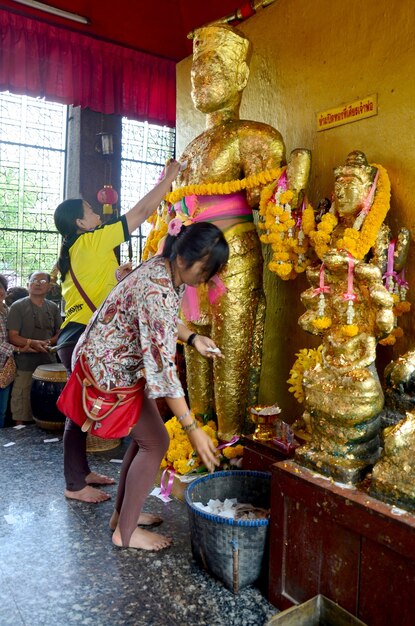 La donna tailandese glid copre la statua dell'angelo con foglia d'oro al Santuario di Phra Kal