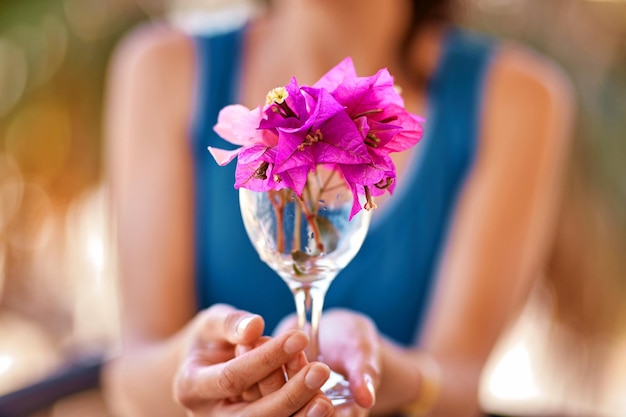 La donna tiene fiori rosa luminosi Bougainvillea in un bicchiere di vino davanti a se stessa Concetto pubblicitario di viaggio e vacanze estive Estate fiori surreali concetto creativo alla moda