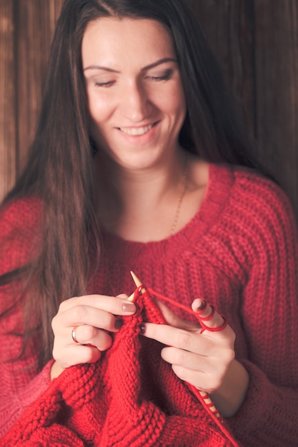 La donna tiene gli aghi e lavora a maglia una giacca calda rossa