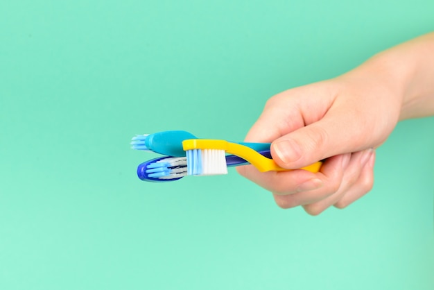 La donna tiene gli spazzolini da denti in mano su uno sfondo verde.