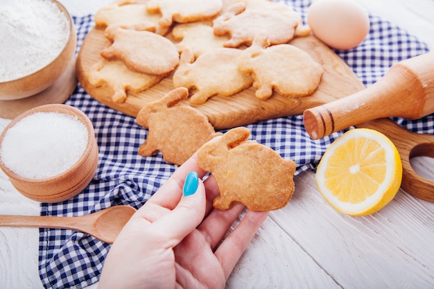 La donna tiene il biscotto a forma di coniglietto di pasqua circondato con gli ingredienti