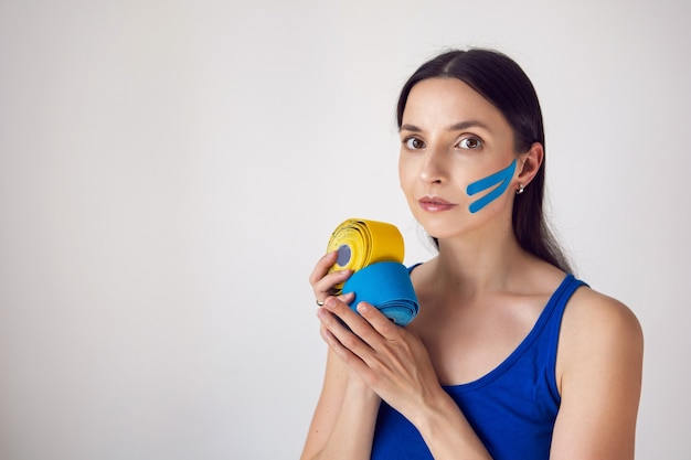 La donna tiene in mano due matasse di nastro kinesio giallo e blu