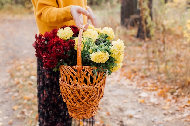 La donna tiene in mano un cesto con fiori autunnali nella foresta
