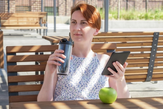 La donna tiene in mano un dispositivo ebook e una tazza di caffè riutilizzabile