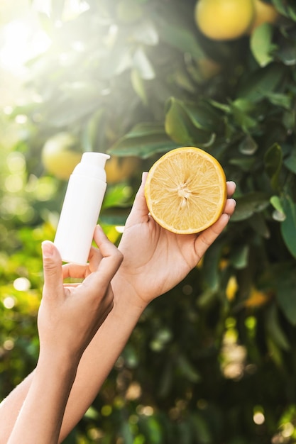 La donna tiene in mano una bottiglia di prodotto per la cura della pelle e metà di limone sullo sfondo dell'albero di limone