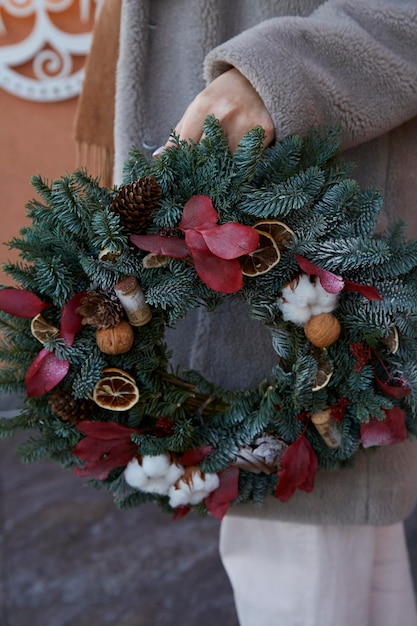 La donna tiene l'estetica festiva corona di Natale all'esterno Accogliente casa festiva decorazioni di Capodanno