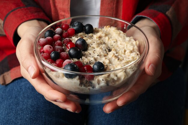 La donna tiene la ciotola con il porridge di farina d'avena con i frutti. Avvicinamento