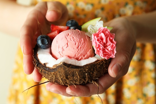 La donna tiene la noce di cocco con il gelato alla frutta, primo piano