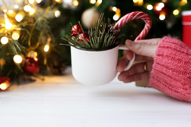 La donna tiene la tazza con palloncini rossi Rami di albero di Natale e lecca-lecca sul tavolo bianco