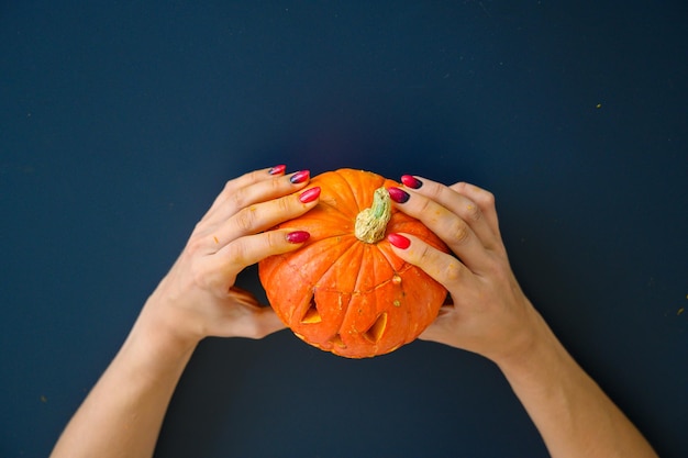 La donna tiene la zucca con la faccia ritagliata per la lampada di halloween sul tavolo nero Primo piano delle mani femminili che fanno jacko39lantern alla vigilia di tutti i santi Vista dall'alto