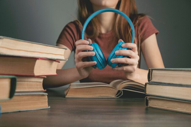 La donna tiene le cuffie mentre è seduta davanti ai libri. concetto di audiolibro