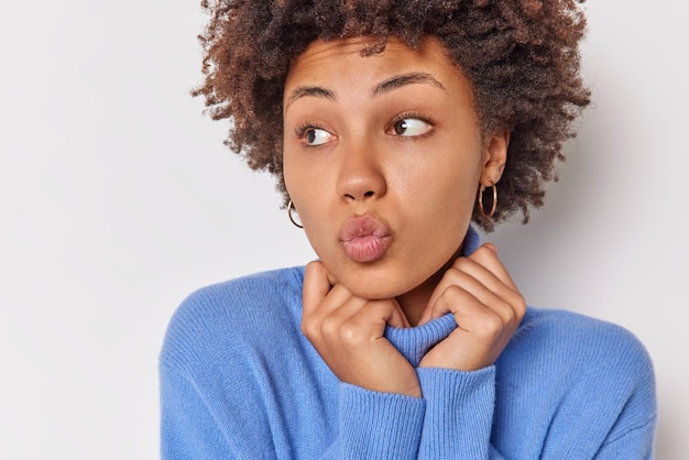 la donna tiene le labbra piegate vuole baciarti vestito con un dolcevita blu casual concentrato lontano isolato su bianco. Modello femminile affettuoso