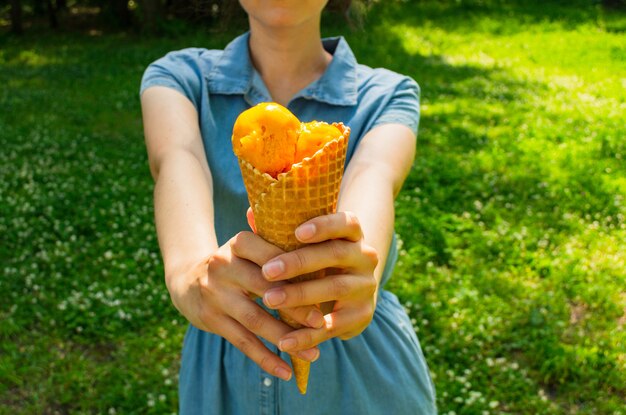 La donna tiene un gelato nelle sue mani. Gelato al mango in un cono di cialda