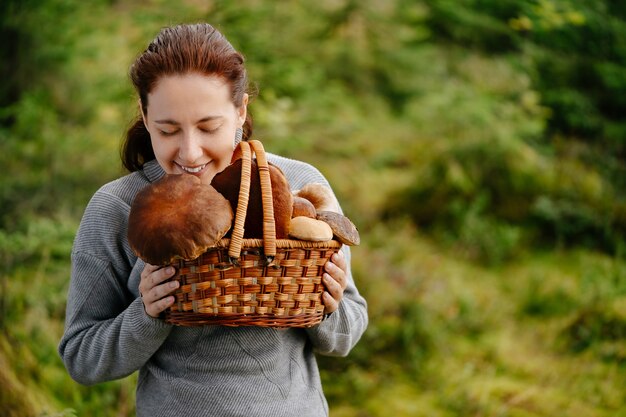 La donna tiene un raccolto di foresta in un cesto di vimini con funghi trovati Concetto di cibo biologico