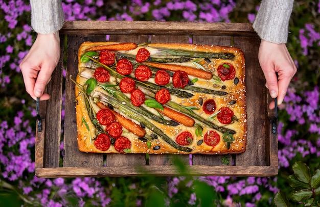 La donna tiene un vassoio di focaccia nel cortile, con fiori