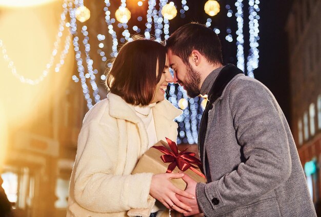 La donna tiene una confezione regalo Felice giovane coppia che celebra il nuovo anno all'aperto per strada