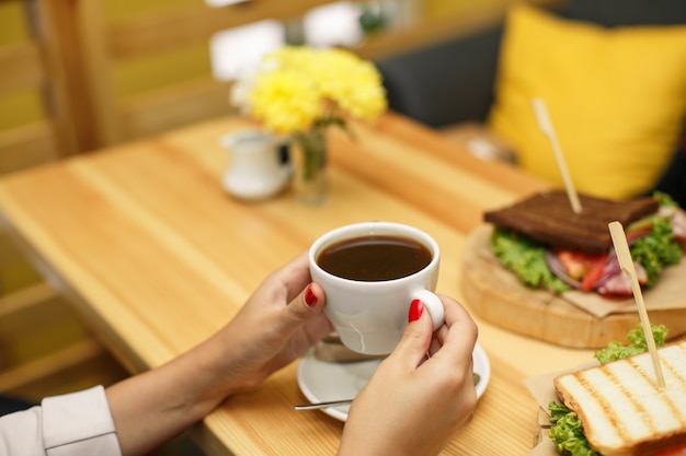 La donna tiene una tazza di caffè al tavolo di legno backgroud, su cui giace un panino