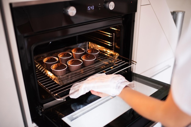 La donna tira fuori dal forno caldo gustosi cupcakes al cioccolato nel vassoio in cucina