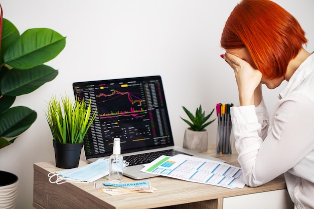 La donna triste sta guardando i grafici di borsa che cadono durante un'epidemia covid-19.