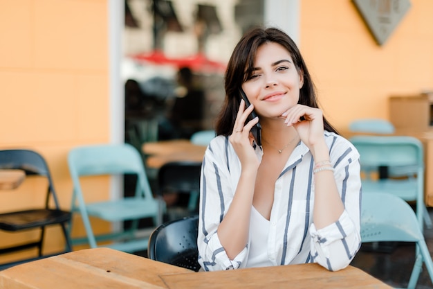 La donna usa il telefono che si siede in caffè all'aperto