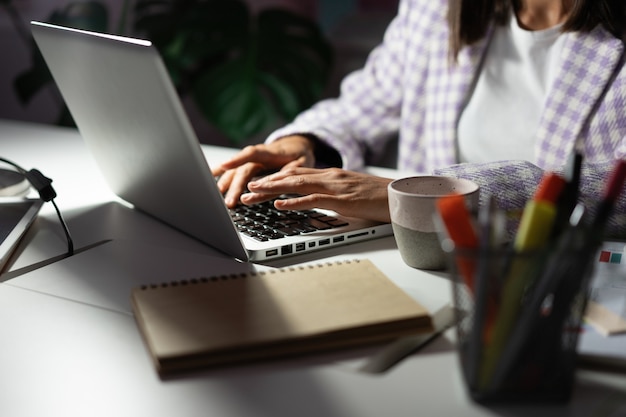 La donna usa un laptop mentre lavora a una nuova idea di progetto a tarda sera. Le mani femminili stanno digitando sulla tastiera del laptop