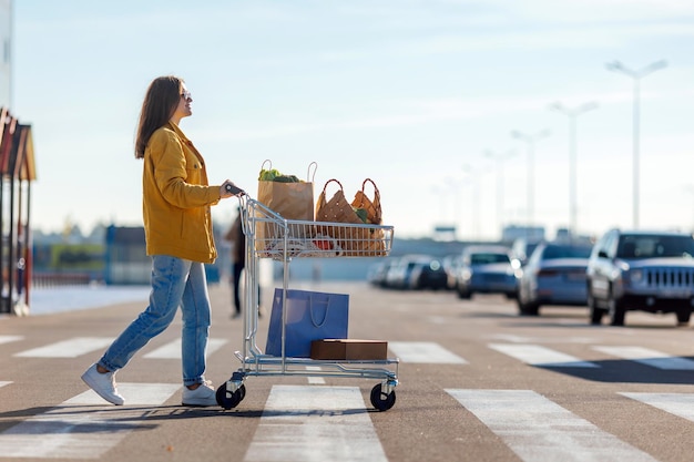 La donna va attraversamento pedonale da un centro commerciale con carrello con generi alimentari