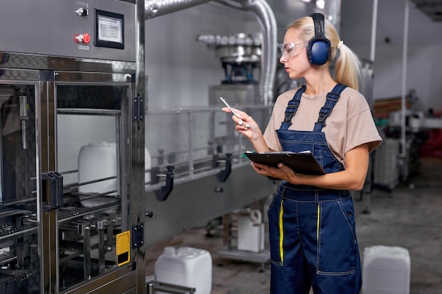 La donna valuta la qualità della produzione di pesticidi in fabbrica, prende appunti, in uniforme