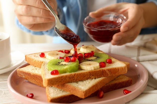 La donna versa la marmellata su gustosi toast con frutta