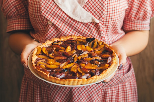 La donna vestita con un vestito tiene in mano un bel piatto con prugne o crostata di prugne.