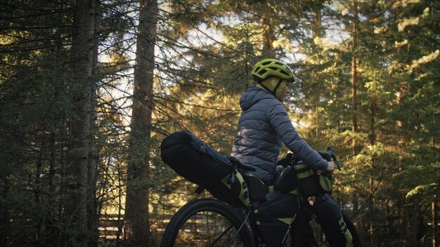 La donna viaggia su terreni misti cicloturismo con bici bikepacking outdoor Il viaggiatore viaggio con borse da bici Elegante bikepacking abbigliamento sportivo da bici nei colori verde nero Magico parco forestale