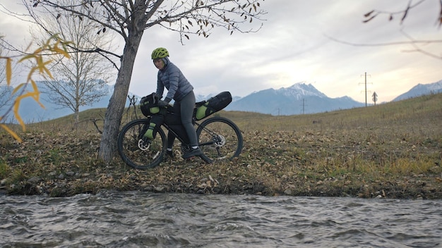 La donna viaggia su terreno misto Cicloturismo con bikepacking Il viaggio del viaggiatore con le borse da bicicletta Abbigliamento sportivo nei colori verde nero Il viaggio nella magica foresta autunnale ruscello