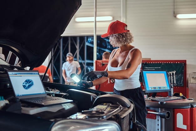 La donna virile concentrata sta eseguendo la diagnostica dell'auto con l'aiuto del computer al servizio automatico.