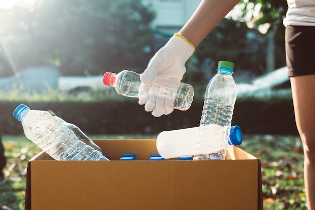 La donna volontaria tiene la bottiglia di plastica nella scatola di carta al parco pubblico, smaltisce il concetto di riciclo e gestione dei rifiuti, buona mente cosciente