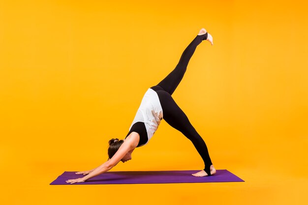 La donna yogi esegue l'asana Adho Mukha Shvanasana su un tappetino viola su una parete arancione