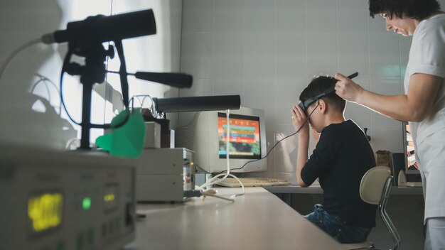 La dottoressa controlla la vista del ragazzo con l'aiuto di occhiali per realtà virtuale stereovideo, grandangolare