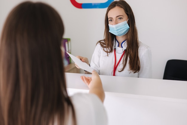 La dottoressa in maschera protettiva dà la carta con la ricetta alla clinica luminosa del cliente