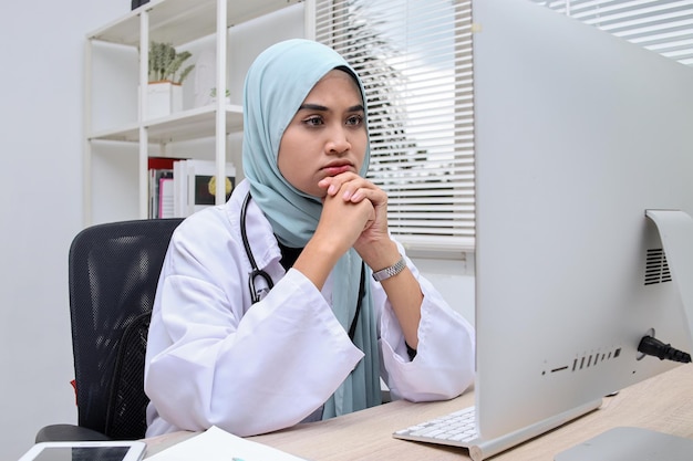 La dottoressa musulmana si siede alla scrivania in ospedale e lavora online sul computer pensando alla soluzione.