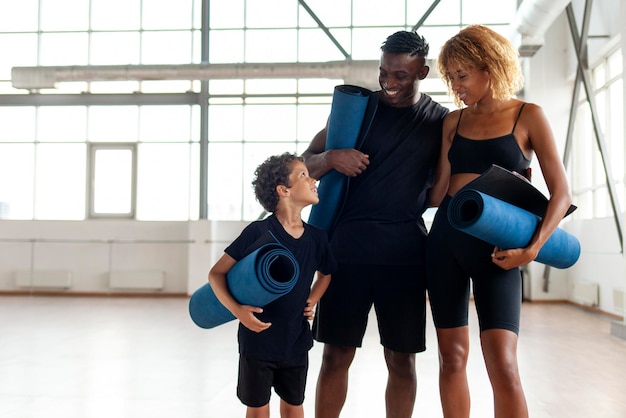 La famiglia afroamericana in abbigliamento sportivo con tappetino da yoga si trova in palestra e sorride mamma papà e figlio